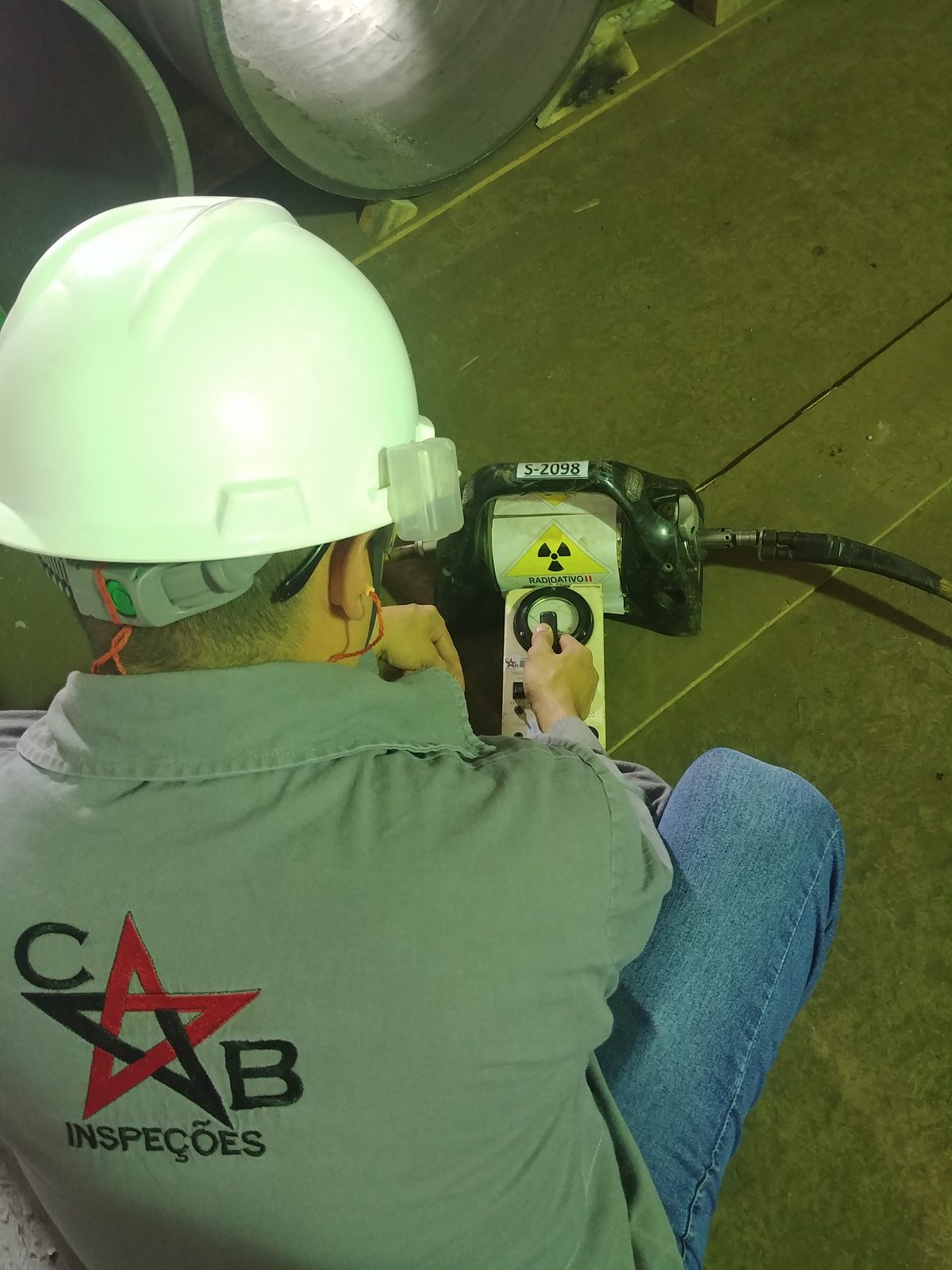 Inspetor com uniforme da CB Inspeções e capacete operando o equipamento de gamagrafia em campo