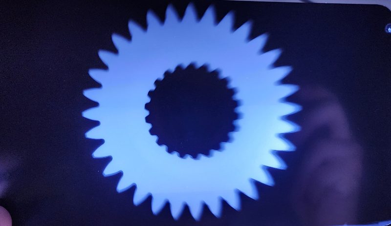 Radiografia de uma engrenagem vista no negatoscópio: dentes e furo estriado central em alto contraste azul